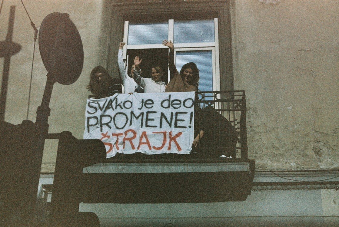 drei Frauen auf einem Balkon mit Schriftzug auf einem Tuch "svako je deo promene, štrajk"